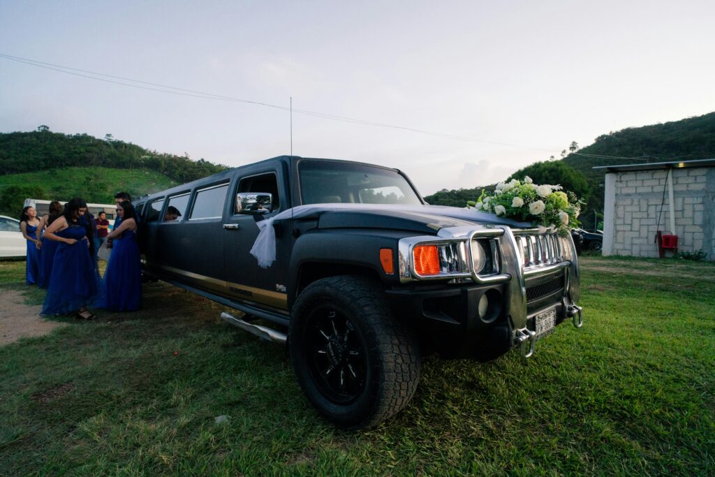 Black limousine adorned with floral wedding decorations parked outdoors with people in the background.