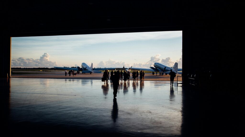 Silhouettes of people walking toward planes at an airport during the day.